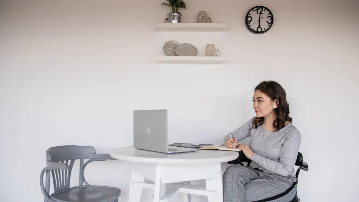 Junge Frau lernt an einem Tisch mit Laptop und Heft